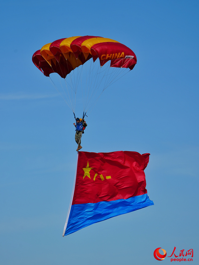 “八一”“藍鷹”跳傘隊攜帶黨旗、國旗、八一軍旗和空軍軍旗先后躍出機艙，而后，多名跳傘